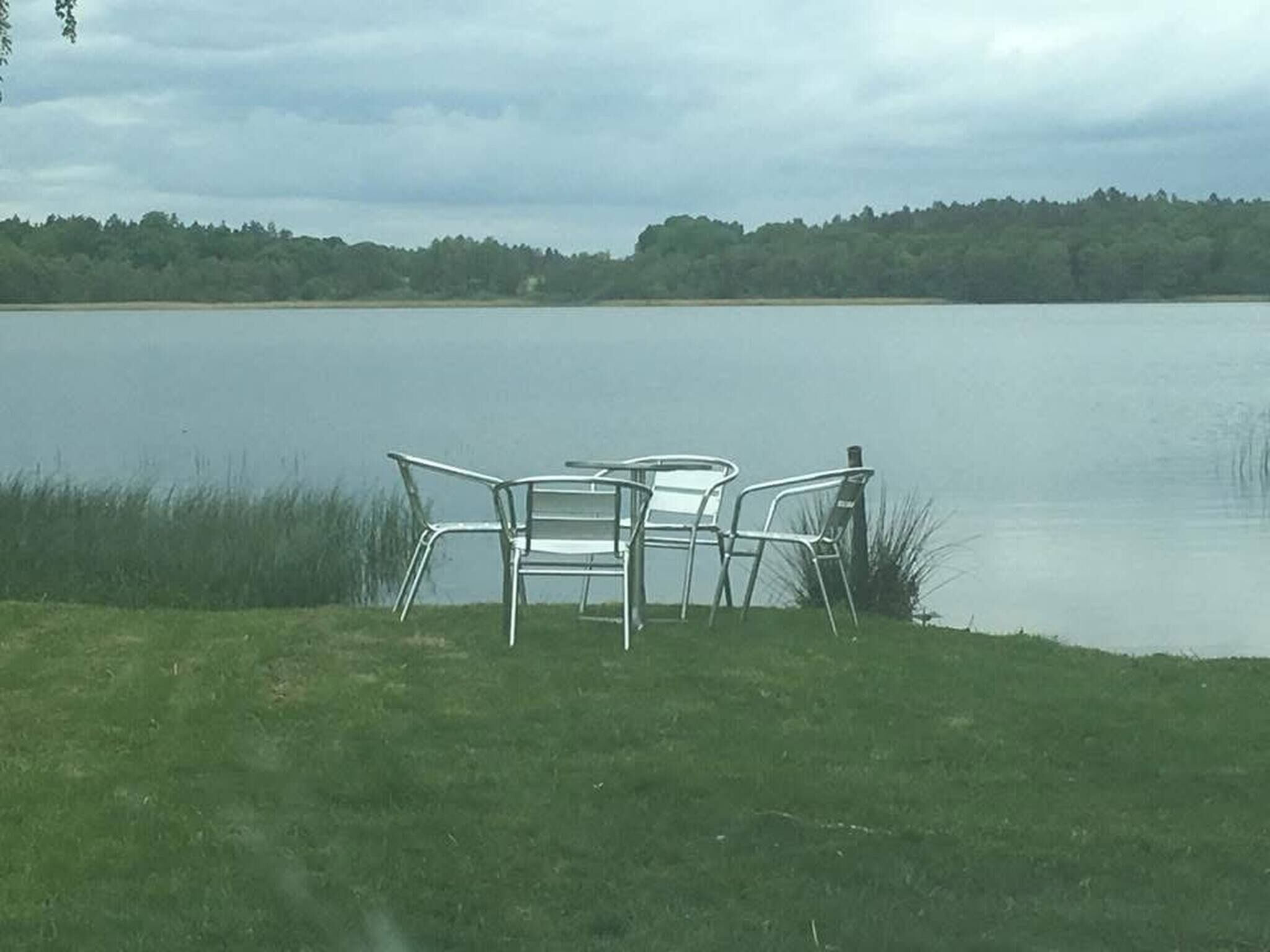Vista para o lago, com duas cadeiras de metal e uma mesa em uma área gramada.