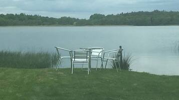 Vista para o lago, com duas cadeiras de metal e uma mesa em uma área gramada.