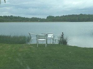Vista a un lago con dos sillas de metal y una mesa en una zona verde.
