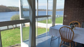 A balcony with a table and chairs, overlooking a lake with a white fence and trees.