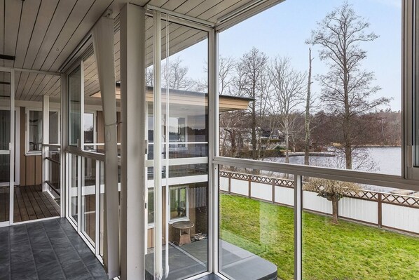 A modern building with large glass windows and a balcony overlooking a grassy area and a body of water.