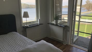 Un dormitorio con una cama, una ventana con vistas a un lago, un radiador y una planta en maceta.