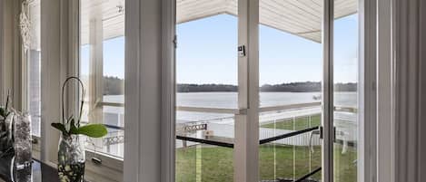 A room with large windows overlooking a body of water and a dock. There are potted plants on a window sill.