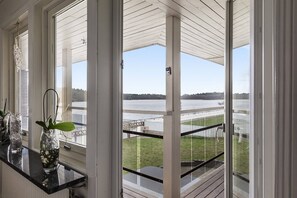 Habitación con ventanas amplias que dan a una masa de agua y un muelle. Hay plantas en macetas sobre el alféizar.