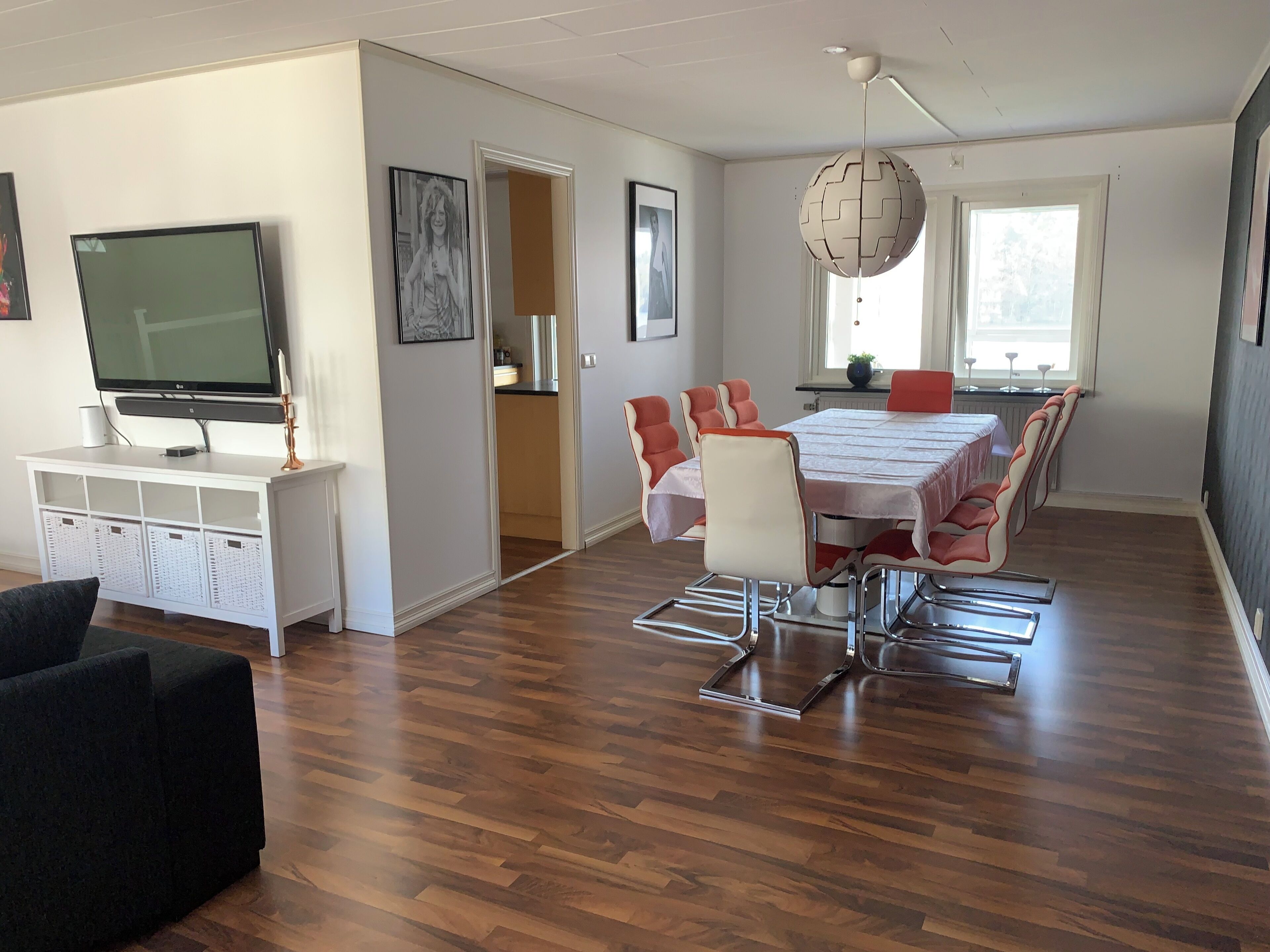 Uma sala de estar moderna com televisão de tela plana, uma mesa de jantar com cadeiras e uma janela grande.