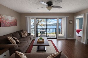 A living room with a sofa, coffee table, and a view of a lake through large sliding glass doors. - Shorefront Escape at TRL (Kimberling City)