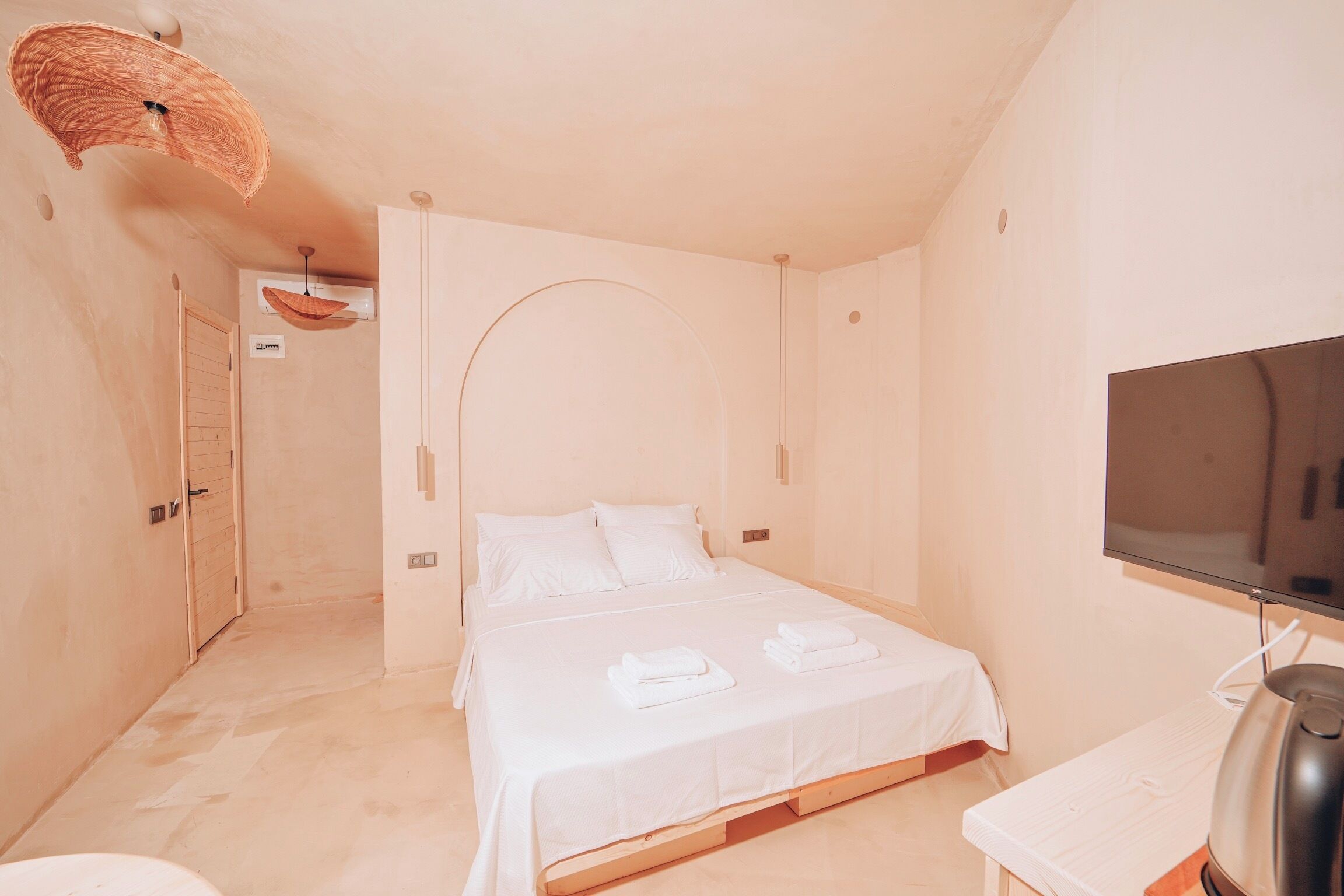 A hotel room with a bed, a television, a kettle, and a door leading to another room.