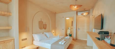A modern bedroom with a bed, bedside tables, a wooden bench, a TV, and a kitchenette area.