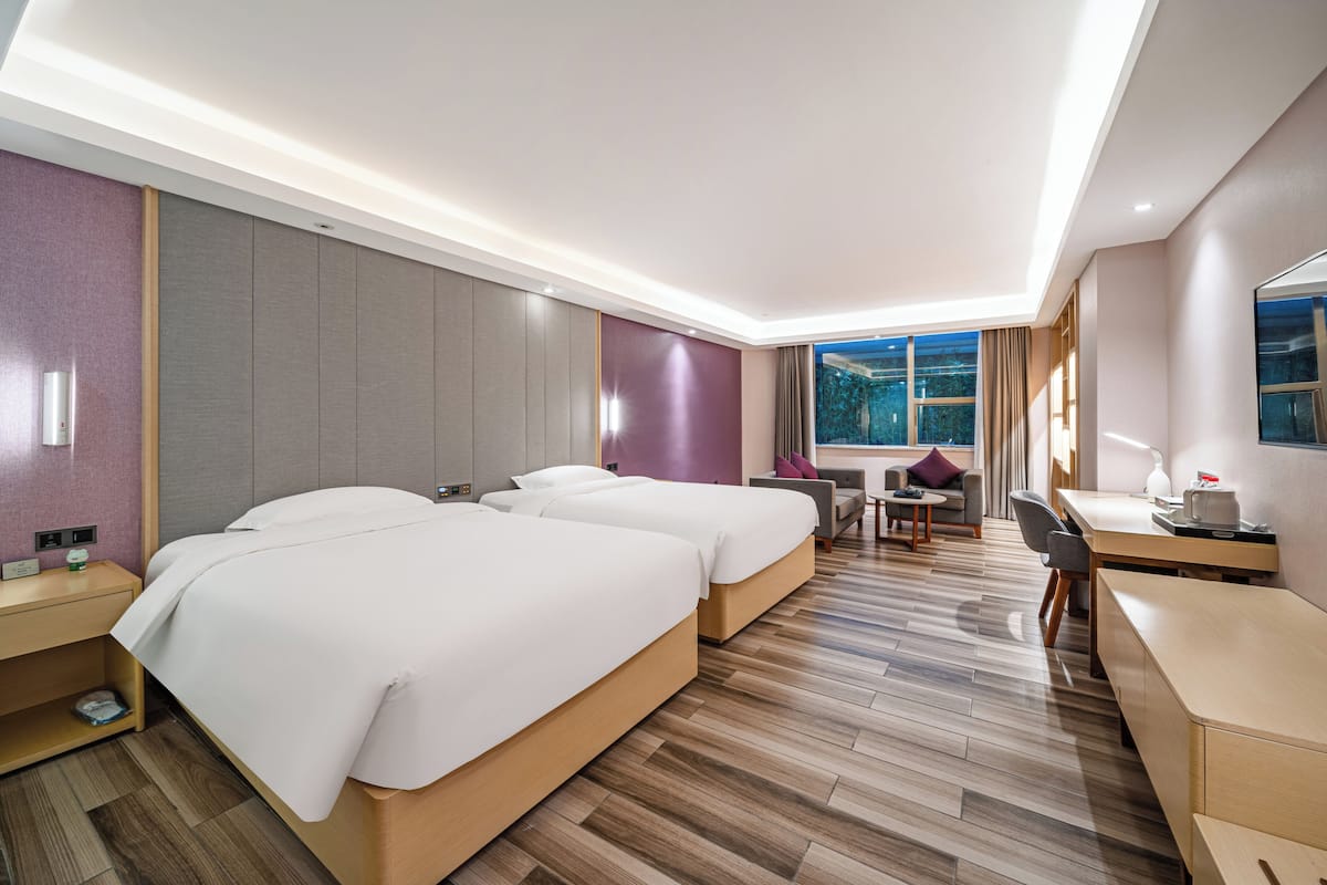 A hotel room with two beds, a desk, a chair, a small table, and a window with a view.