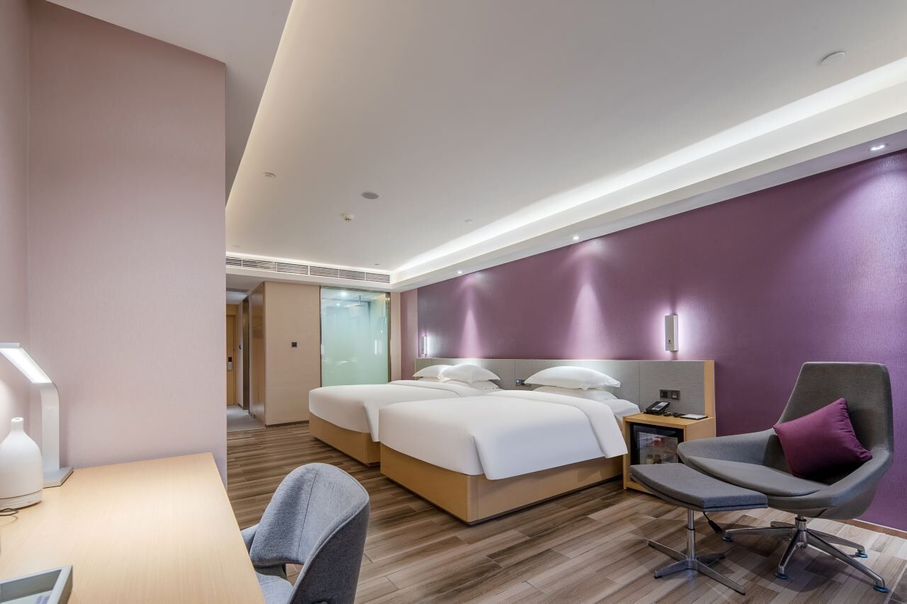 A modern hotel room with two beds, a desk, and a chair.