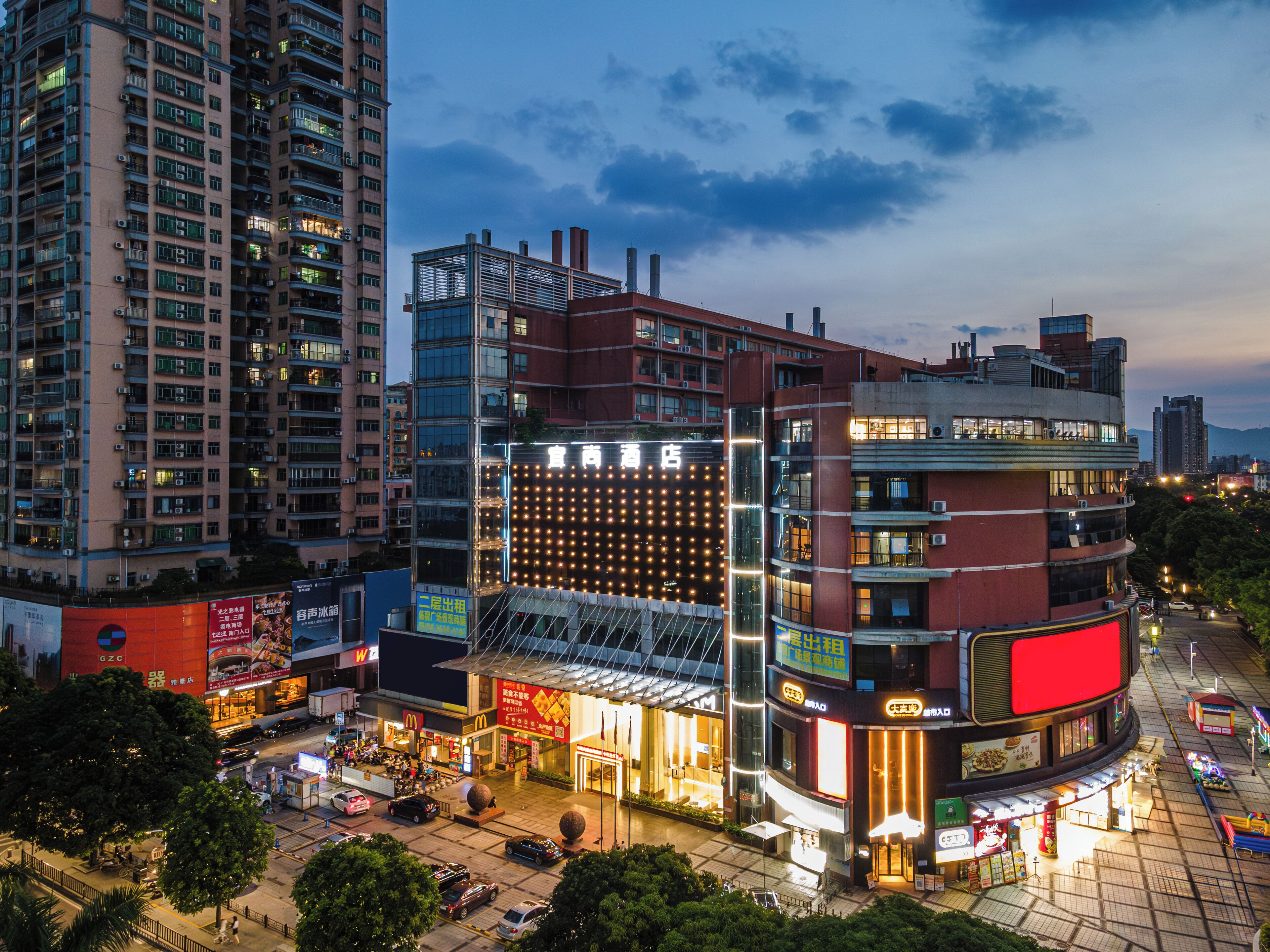 A multi-story hotel with a prominent glass facade, a rooftop terrace, and a ground-level restaurant.