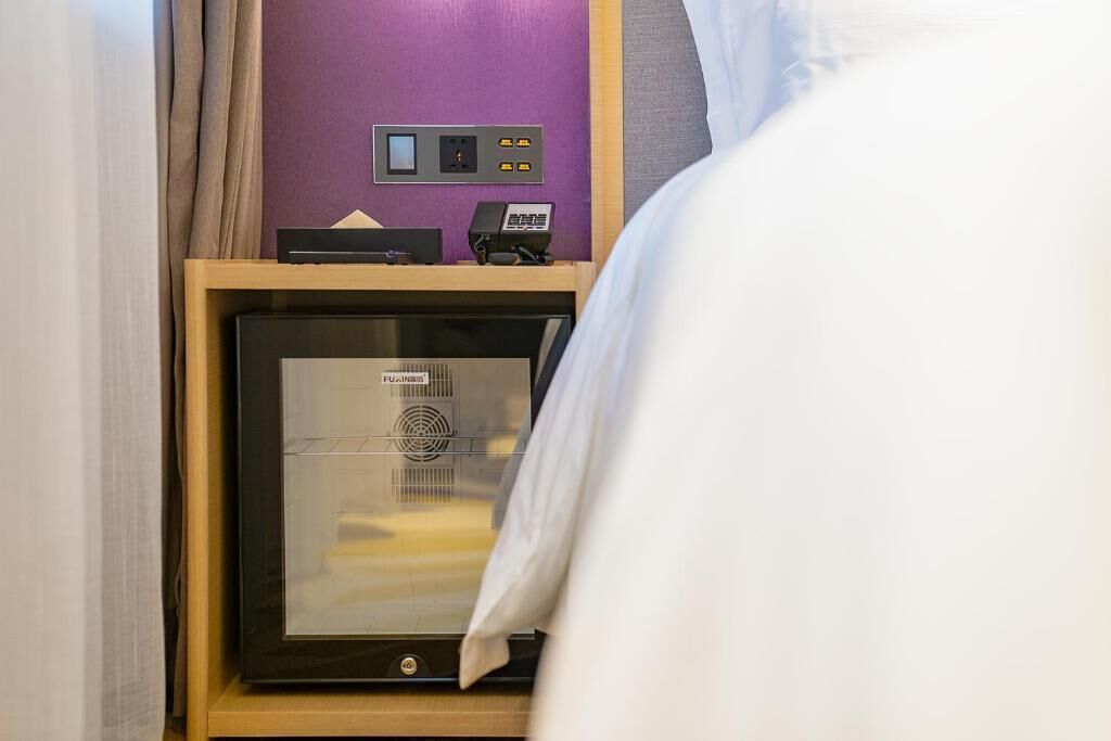 A room with a bed, a framed picture, a control panel, and a purple wall.