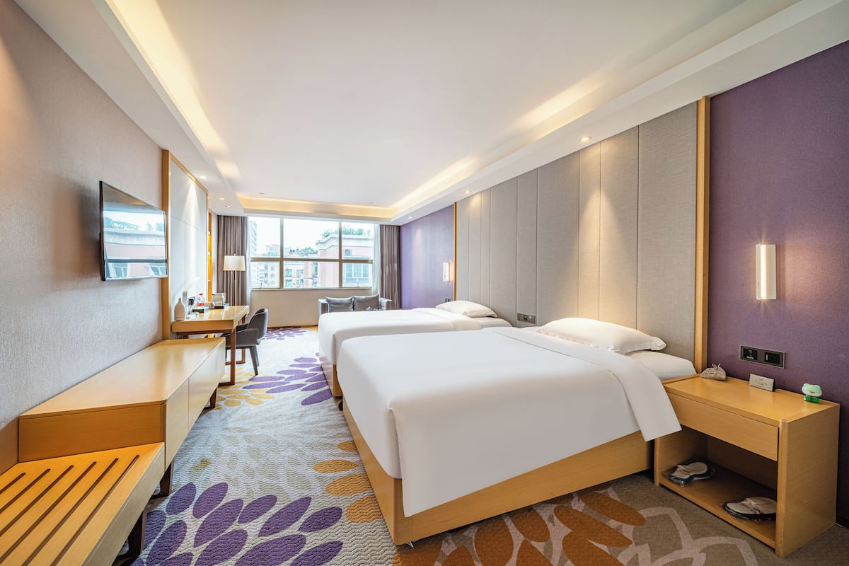 A hotel room with two beds, a desk, a chair, a TV, and a window with a city view.