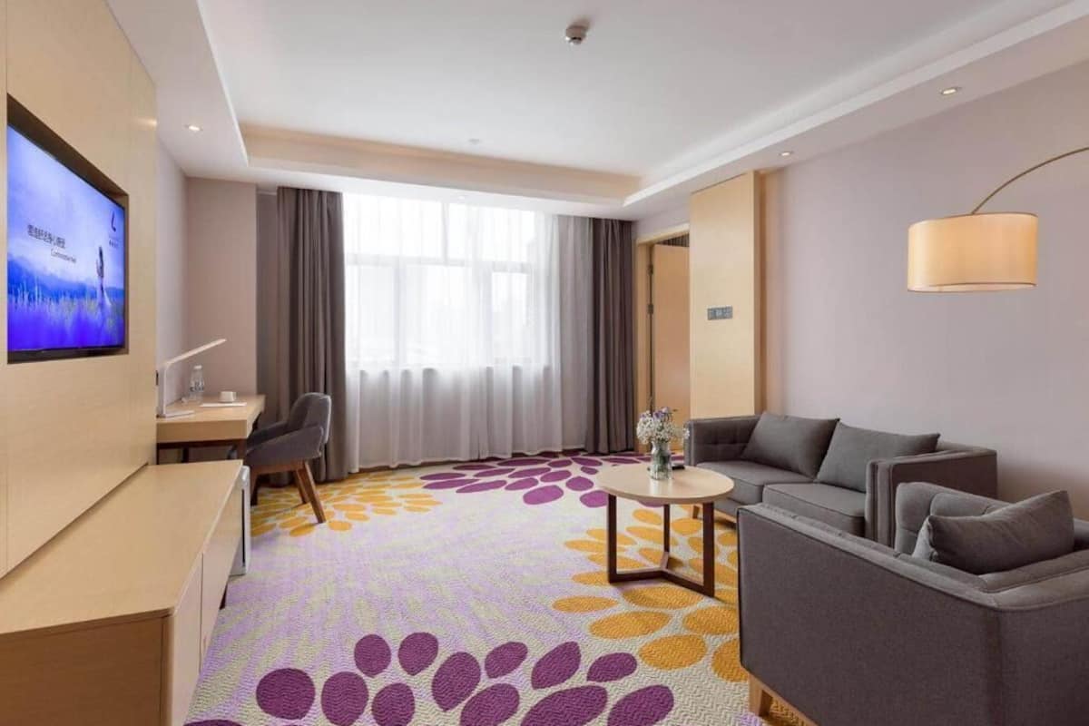 A hotel room with a sofa, a TV, a desk, and a patterned carpet.