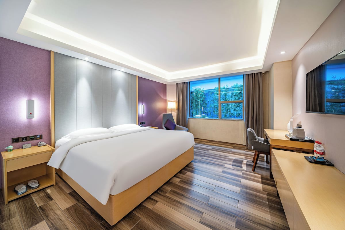 A modern hotel room with a large bed, a desk, a chair, and a view of the outdoors.