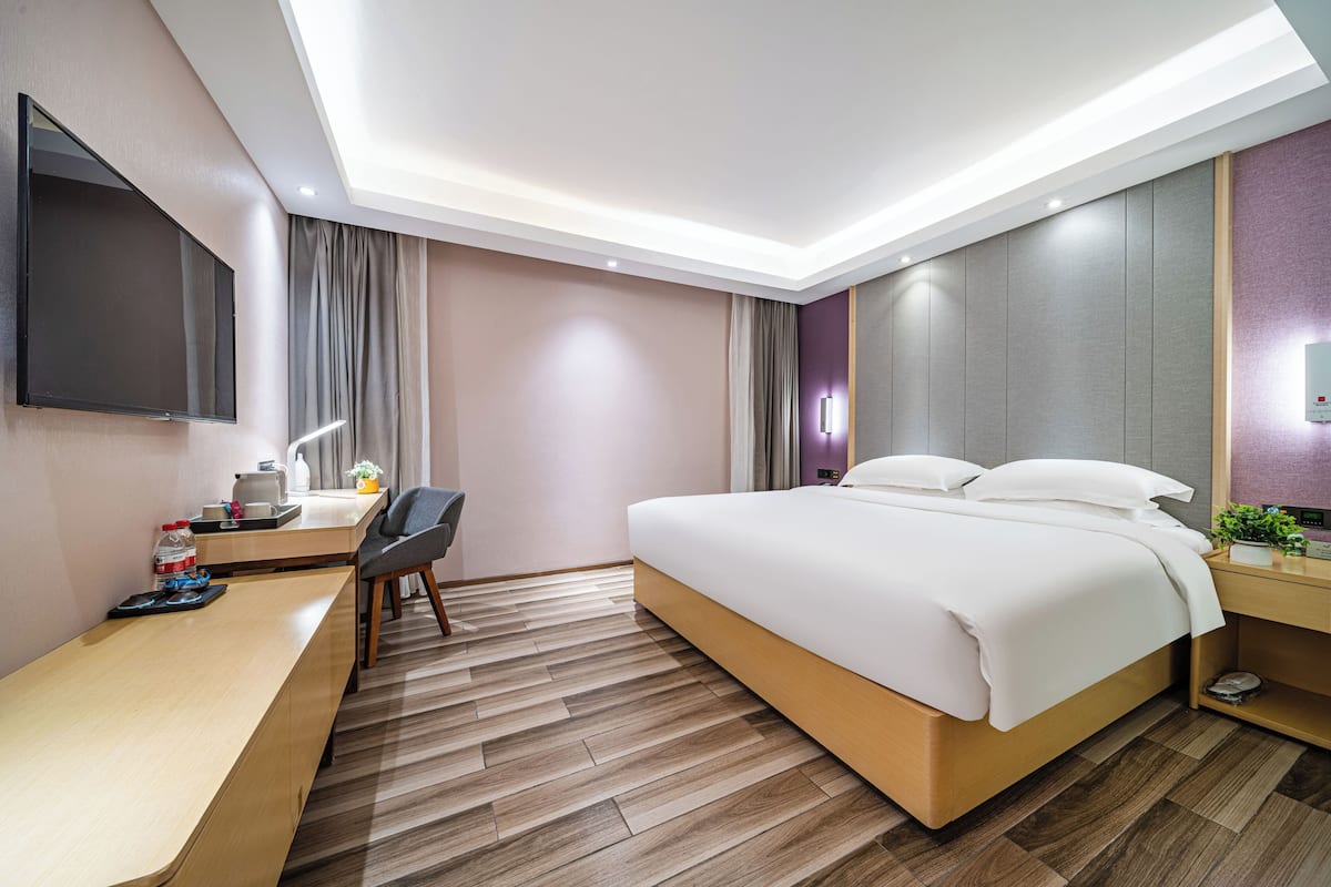A modern hotel room with a large bed, a desk, a flat-screen TV, and a ceiling light.