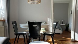 Un salon moderne avec un coin repas, comprenant une table ronde, des chaises noires, un luminaire suspendu et une petite table d’appoint avec des blocs.