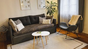 Un salon avec un canapé foncé, une petite table ronde, un fauteuil à bascule et une plante en pot.