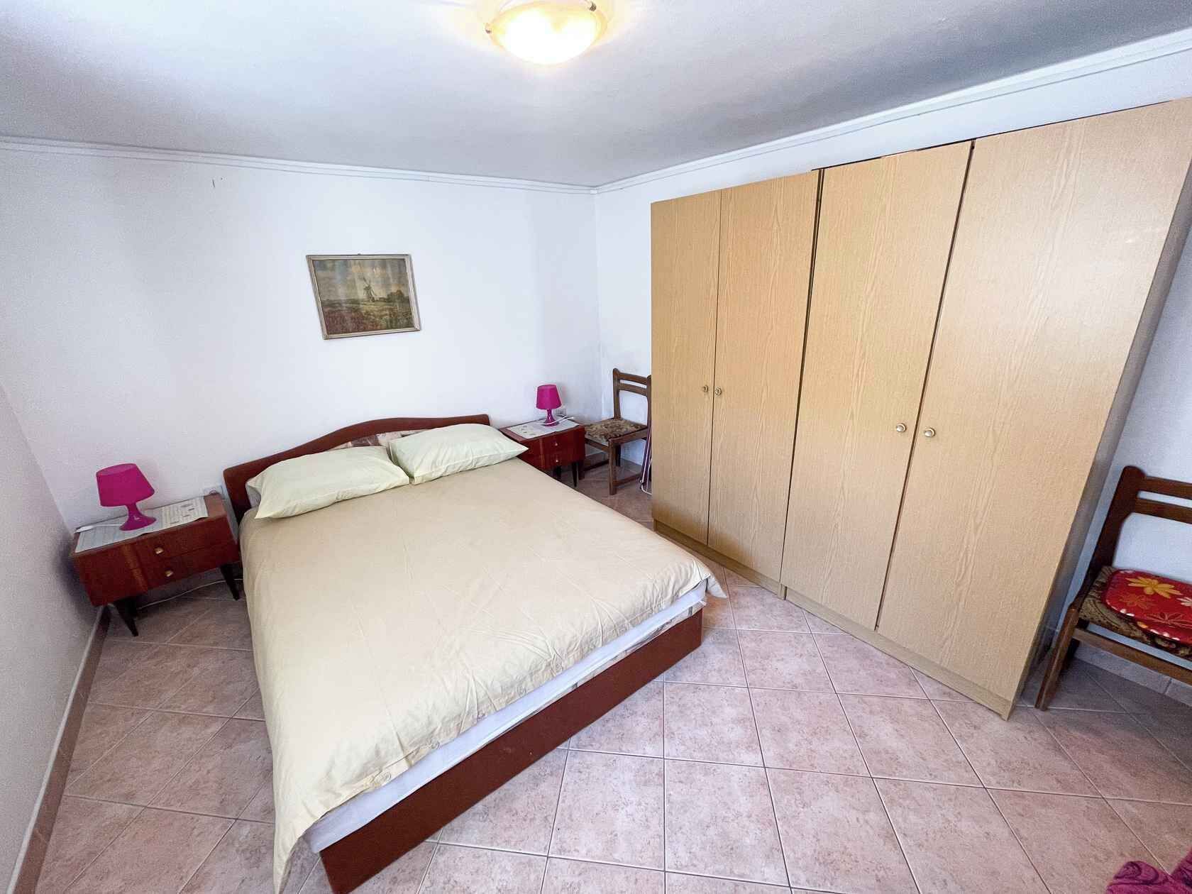 A bedroom with a bed, a wardrobe, a nightstand, a chair, and a wall-mounted lamp.