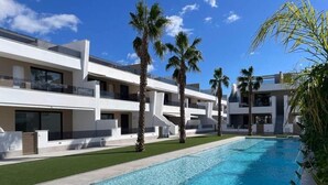 A modern hotel with a swimming pool, palm trees, and a clear blue sky.