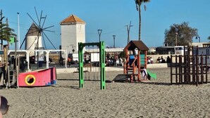 A beach with a windmill, playground, and a building with a red roof.