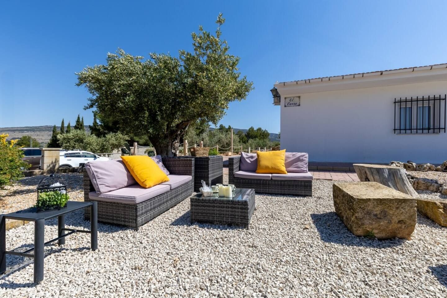 Un espace extérieur aménagé avec des meubles et des coussins en osier, une table avec une bougie et un banc en pierre.