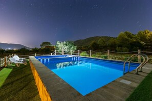 A rectangular swimming pool with a metal ladder on one side, surrounded by a wooden fence and a grassy area with lounge chairs.