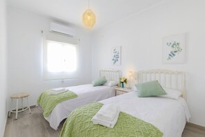 A room with two beds, a window, an air conditioning unit, and a hanging light fixture.