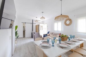 Un espace repas moderne avec une table blanche dressée pour six personnes, entourée de chaises.