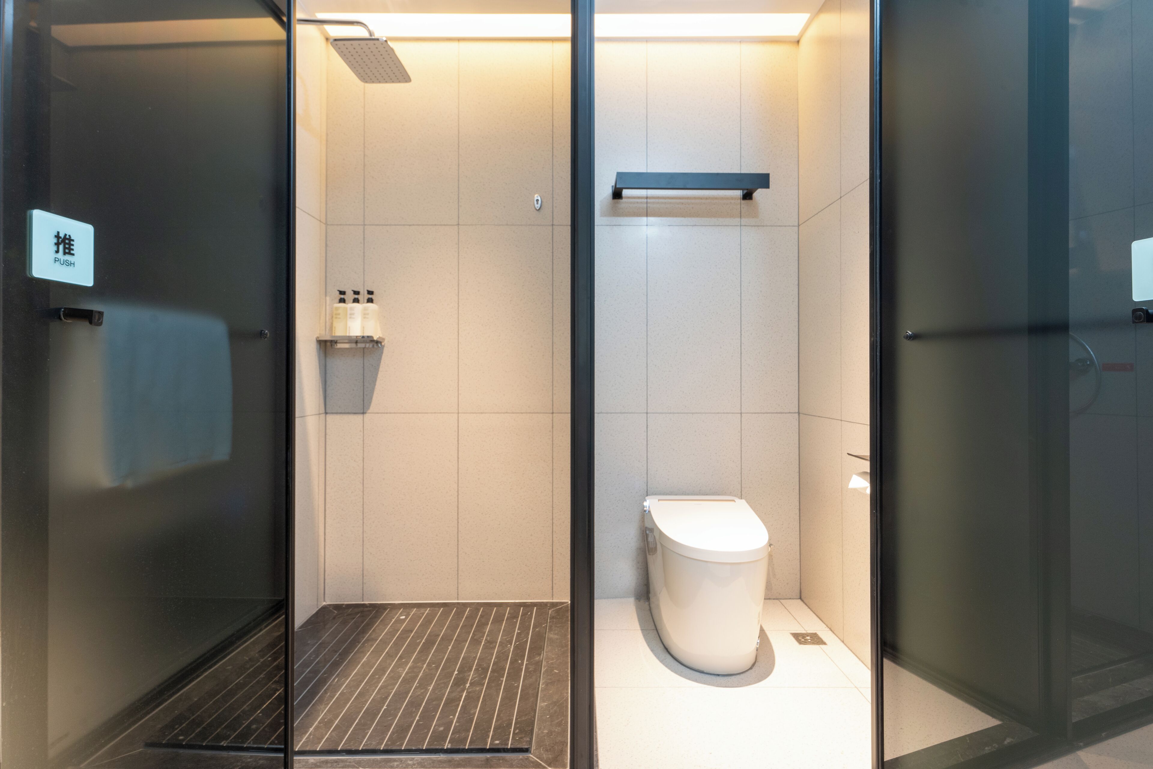 Een moderne badkamer met een glazen deur, een wit toilet en een plank met toiletartikelen.