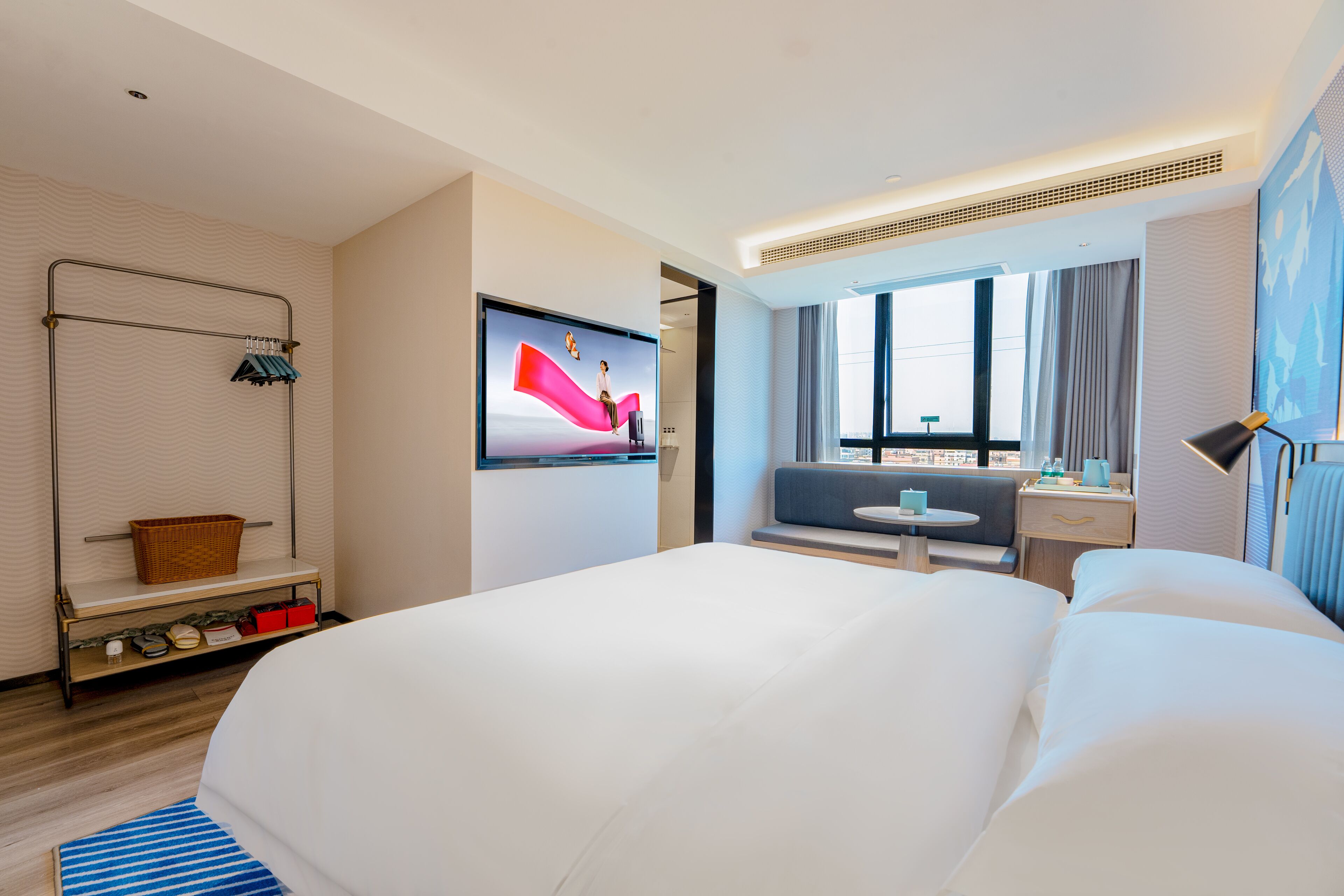 A modern hotel room with a large bed, a television, a seating area with a table, and a window with curtains.