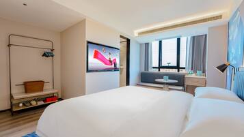 A modern hotel room with a large bed, a television, a seating area with a table, and a window with curtains.
