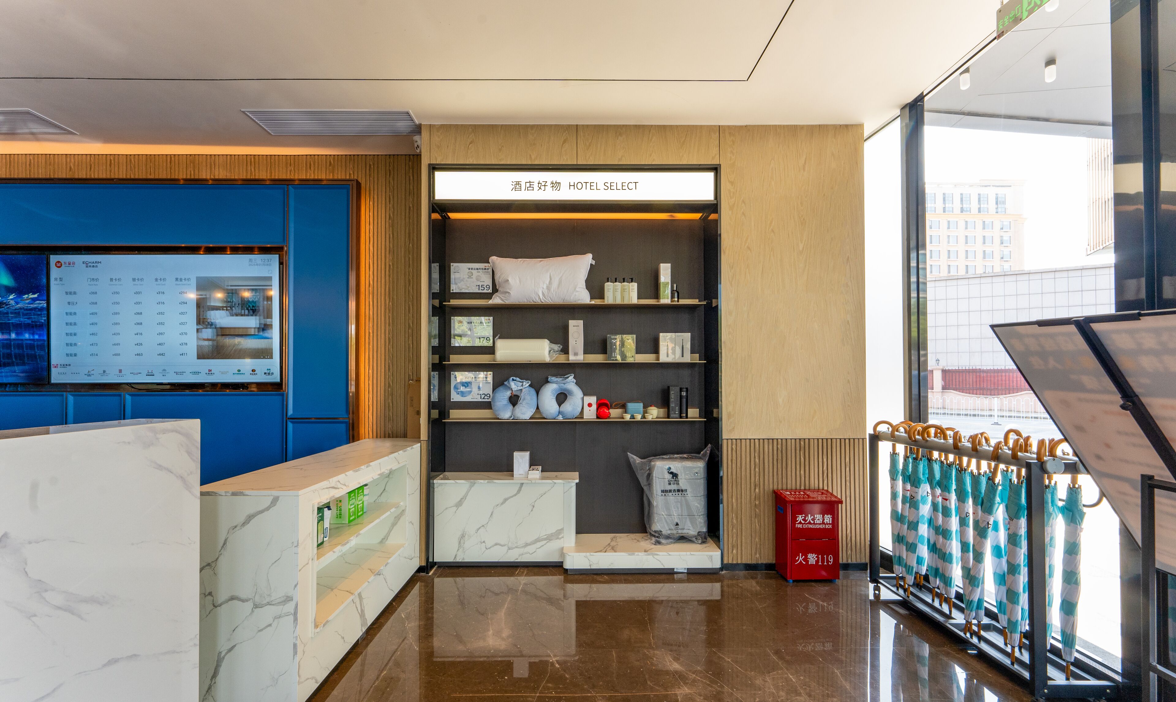 Uma área de recepção de hotel com parede azul, balcão de atendimento, exposição de serviços do hotel e vista da cidade através de amplas janelas.
