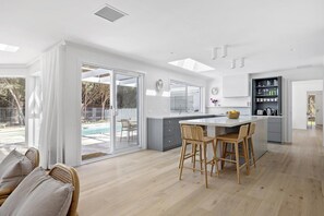 Una cucina moderna con una grande isola, porte scorrevoli in vetro che danno su una piscina e una zona pranzo con sedie in vimini.