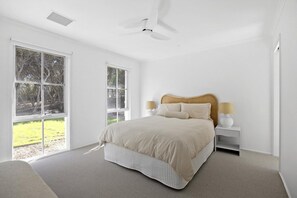 Una camera da letto con un letto, due comodini, una ventola a soffitto e ampie finestre.