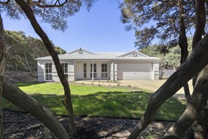 Una casa de un nivel con garaje, rodeada de árboles y un césped cuidado.