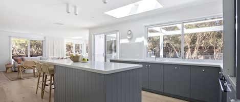 Una cocina moderna con una isla central, ventanas amplias y un comedor con sillas de mimbre.