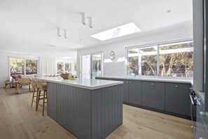 Una cucina moderna con isola centrale, ampie finestre e zona pranzo con sedie in vimini.