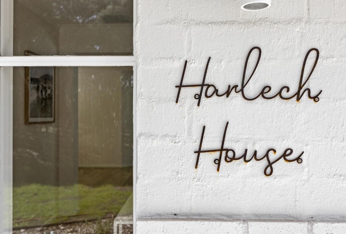 Eine weiße Wand mit der Aufschrift 'Harlech House' in einer verspielten, metallischen Schrift.