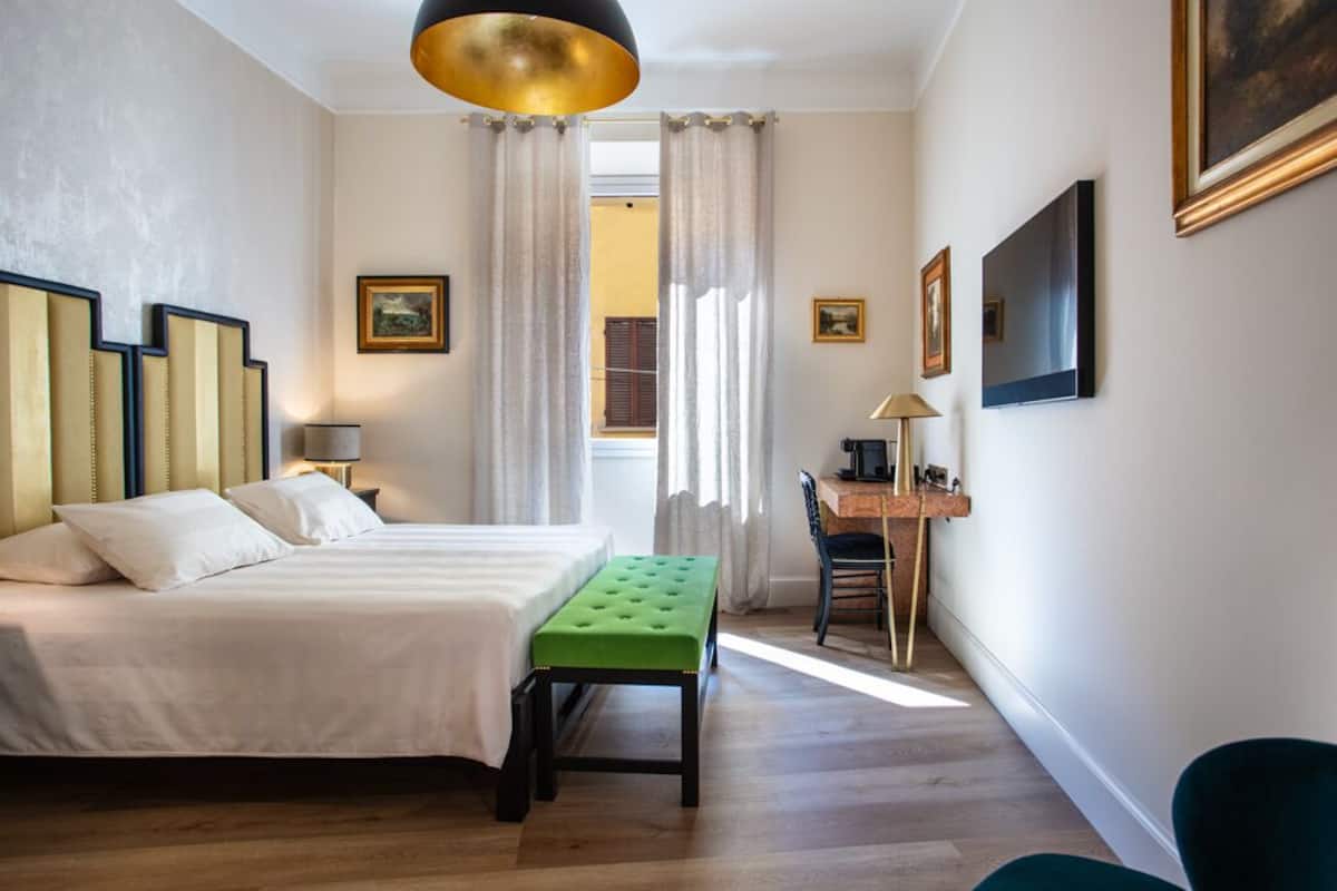 Hotellihuone, jossa on sänky, työpöytä, vihreä rahi ja suuri ikkuna, jossa on verhot.