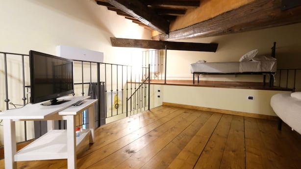 Una habitación con piso de madera, un escritorio blanco con televisor, una litera y una escalera.