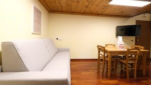 Una habitación con sofá, mesa de comedor de madera, sillas, televisor de pantalla plana montado en la pared y techo de madera.