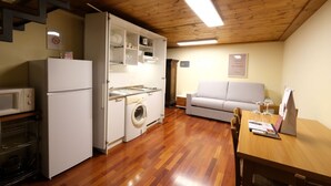 Cocina compacta con lavadora, microondas y refrigerador. Hay un sofá y una mesa de comedor con un menú.