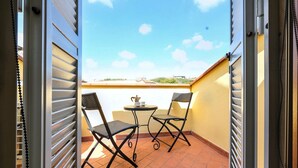 A balcony with two chairs and a small table, featuring a clear view of the sky and distant buildings.