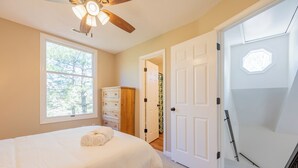 A bedroom with a bed, a ceiling fan, a window, a dresser, and a door leading to another room.