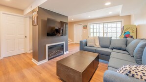 A living room with a fireplace, a grey sofa, and a flat-screen TV mounted on the wall.
