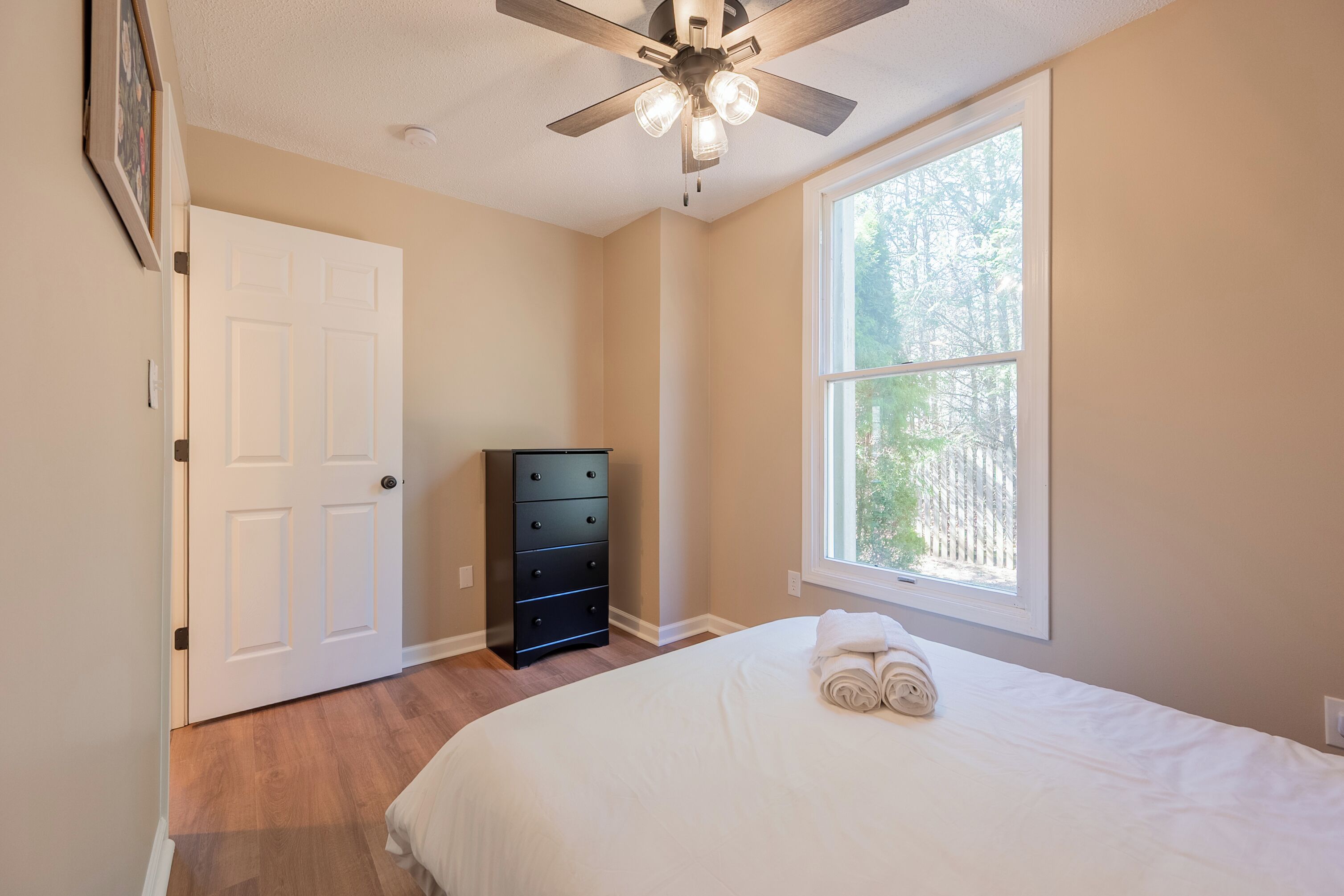 A bedroom with a bed, a dresser, a ceiling fan, a window, and a door.