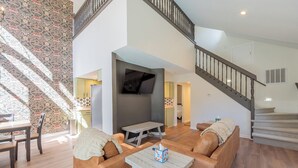 A spacious living area with a sofa set, a coffee table, and a TV mounted on the wall.