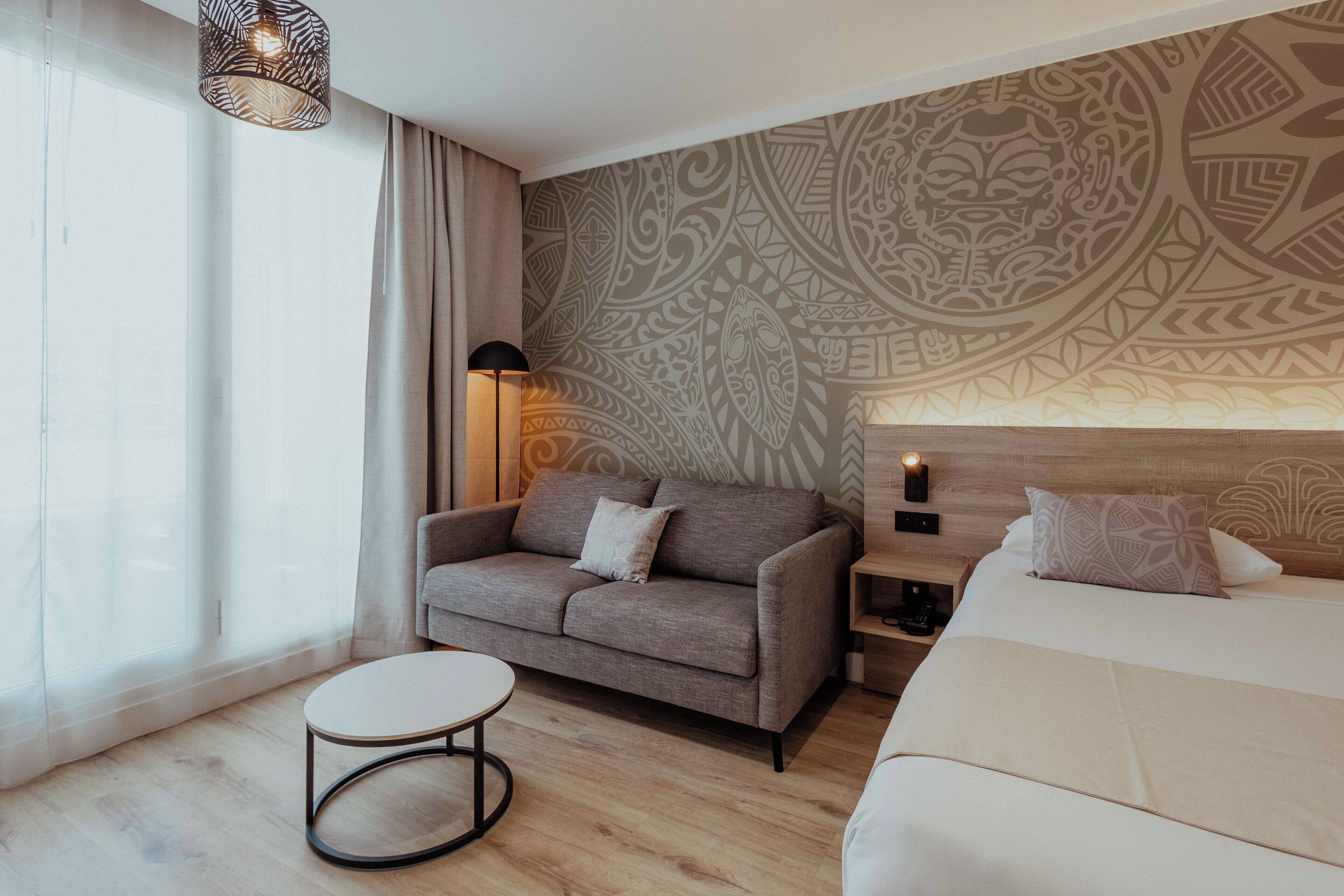 Una habitación de hotel moderna con un sofá, una mesita redonda, una cama y una pared estampada.