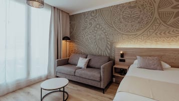 Una habitación de hotel moderna con un sofá, una mesita redonda, una cama y una pared estampada.